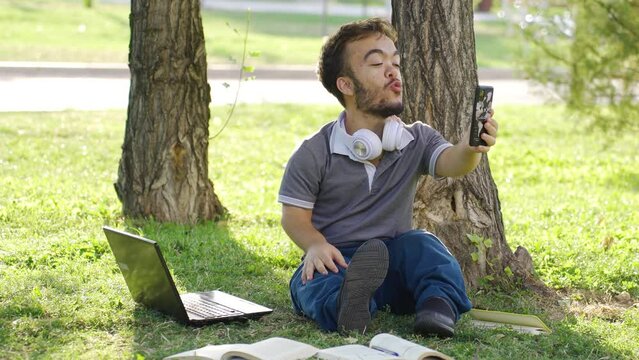 A male college dwarf student is chatting face time with his girlfriend in the park.