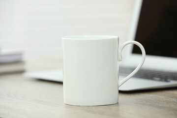 White ceramic mug and laptop on wooden table indoors