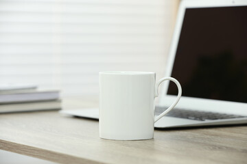 White ceramic mug and laptop on wooden table indoors
