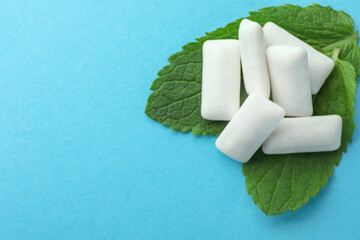 Tasty white chewing gums and mint leaves on light green background, above view. Space for text