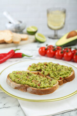 Delicious sandwiches with guacamole and ingredients on white table