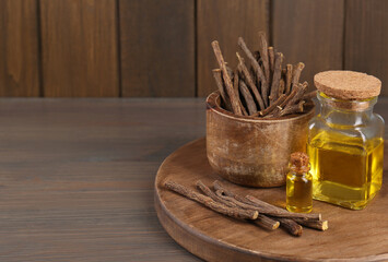 Dried sticks of licorice roots and essential oil on wooden table. Space for text