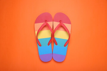 Rainbow flip flops on orange background, flat lay. LGBT pride