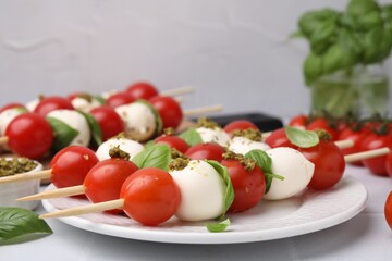 Caprese skewers with tomatoes, mozzarella balls, basil and pesto sauce on table, closeup. Space for text