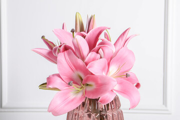 Beautiful pink lily flowers in vase against white wall, closeup