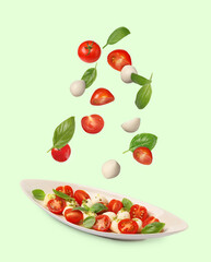 Fresh tomatoes. mozzarella cheese and basil leaves falling onto plate with Caprese salad against pale green background