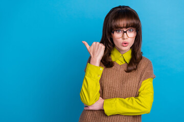 Photo of astonished woman with vintage hair dressed knitwear jumper directing at proposition empty space isolated on blue color background