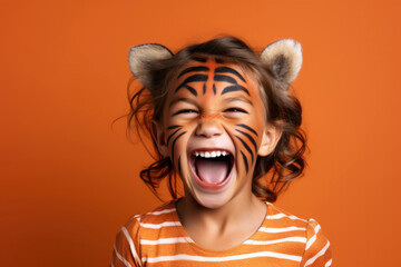 Laughing child with face painted like a tiger on a solid orange background.