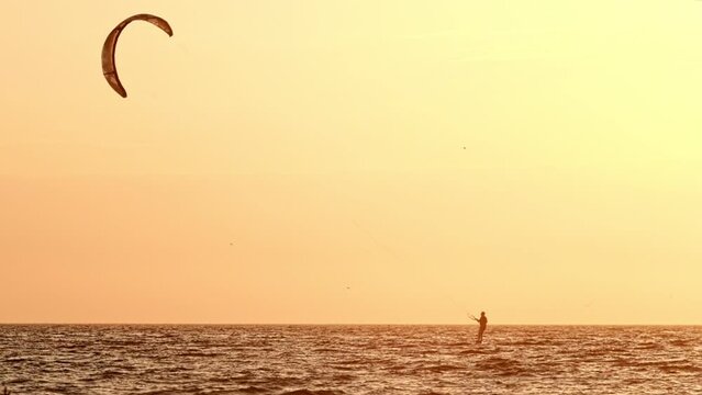 Foiling kiteboarding kitesurfing kiteboarder (kitesurfer) silhouette in the Atlantic ocean on sunset. Fonte da Telha beach, Costa da Caparica, Portugal. Slow motion