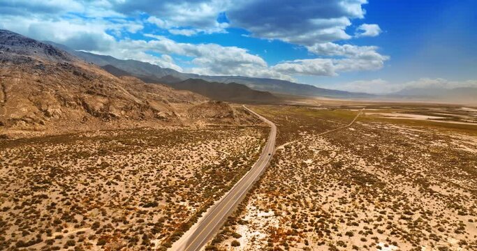 Lonely car moving by the empty highway in hot desert of Death Valley, California. Panorama of a dry desert and mountains from top view.