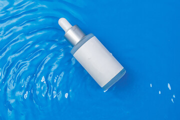 Facial essence bottle mockup. Serum to moisturize the skin. The bottle lies on a blue background in the waves. A daily treat for healthy skin. Anti edge cosmetics
