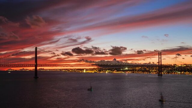 Time-lapse of 25 de Abril Bridge famous tourist landmark of Lisbon connecting Lisboa and Almada on Setubal Peninsula over Tagus river in the evening twilight. Lisbon, Portugal. Zoom in effect