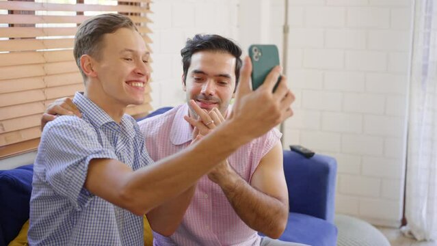 Caucasian attractive gay couple using phone video call in living room.