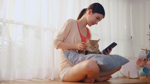 Caucasian young woman using mobile phone with domestic cat at home. 