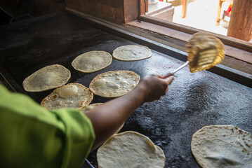 Mexican woman making flour tortillas by hand in front of a comal in a rustic Mexican food restaurant