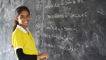 Happy Rural School Girl wearing School Uniform Standing in Front of A Black Board.
