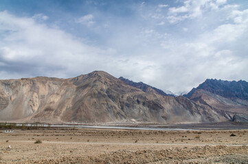 Fototapeta premium Scenic view of Himalayas and Ladakh ranges. Beautiful barren hills in Ladakh with dramatic clouds in the background. View from the road from Nubra Valley to Turuk. Siachen area in Leh Ladakh.