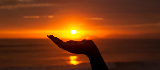 Silhouette of a hand holding the sun, in front of the sea at sunset. Sunbeam. Space for text