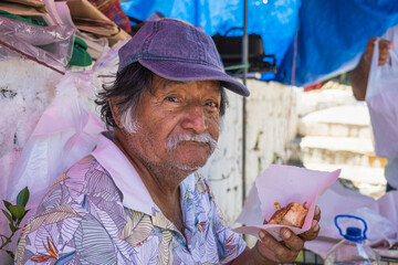 Old latino man posing and eating sweet bread in El Salvador, typical food of El Salvador. With sweet bread in the foreground