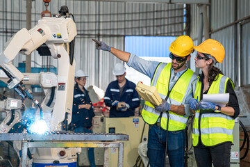 Team of Engineers is controlling robot arm machine welding steel, worker using forcing welding with a control screen which is used for precision welding control.