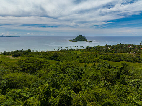 Aerial view of tropical island with green trees under clear sky and clouds. Davao Oriental, Philippines.