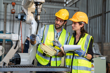 Team of Engineers is controlling robot arm machine welding steel, worker using forcing welding with a control screen which is used for precision welding control.