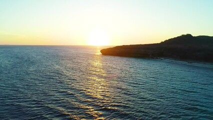 Aerial dolly to setting sun along shimmering golden light on tropical caribbean island coastal waters