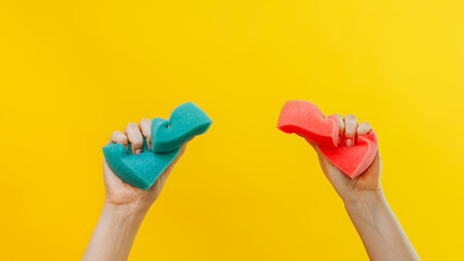 House chores. Domestic cleaning. Janitor services. Woman hands squeezing green pink washing sponges on isolated on yellow background copy space. - obrazy, fototapety, plakaty