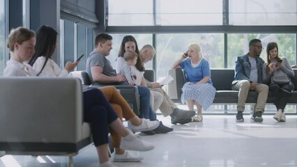 Diverse multicultural people sit on couches in clinic lobby area, wait for appointment with doctor or medical test results. Waiting area in medical center with modern design. Healthcare system.