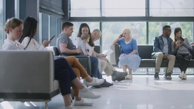 Diverse multicultural people sit on couches in clinic lobby area, wait for appointment with doctor or medical test results. Waiting area in medical center with modern design. Healthcare system.