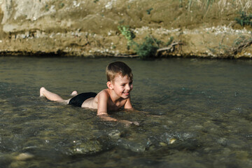 Fototapeta premium a preschool-age boy in bathing trunks plays sitting in the river