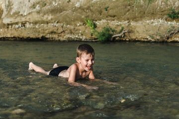 Fototapeta premium a preschool-age boy in bathing trunks plays sitting in the river
