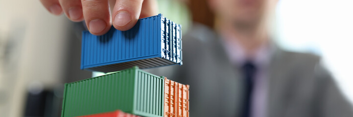 Business man arranging stack of cargo containers on his office desk.