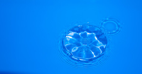 Close up image of water droplets falling into blue water