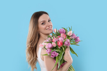 Obraz na płótnie Canvas Happy young woman with bouquet of beautiful tulips on light blue background