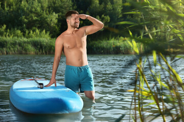Fototapeta premium Man standing near SUP board in river water on sunny day