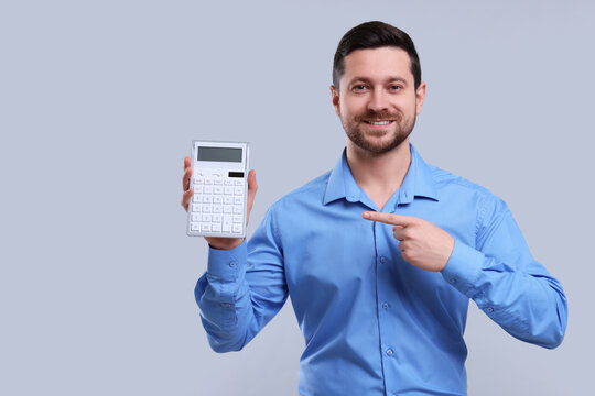 Happy accountant showing calculator on light grey background. Space for text