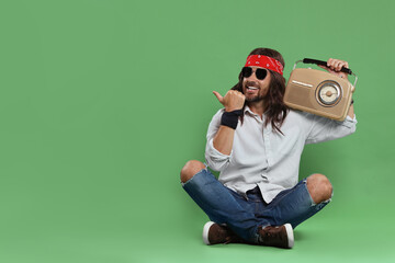 Stylish hippie man with retro radio receiver pointing at something on green background, space for...