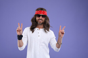 Stylish hippie man in sunglasses showing V-sign on violet background