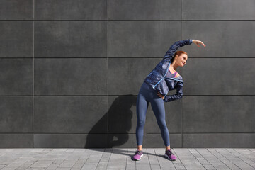 Beautiful woman in gym clothes doing exercises on street, space for text