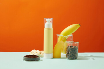 A yellow pump bottle unlabeled with lab glassware container bananas, banana slices, coffee beans and coffee powder on orange background. Minimal concept for organic cosmetic