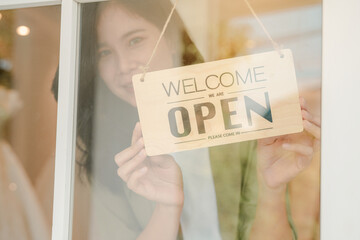 Woman hanging open sign on door, Store owner turning open sign broad through the door glass and...