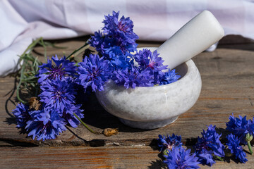 A blue cornflower petal in a vase for medical and cosmetic products. Grind the cornflower flowers in a mortar.  A bunch of cornflowers collected in a bowl. Freshly cut cornflowers. Selective focus.