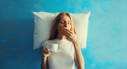 Lazy woman waking up after sleeping and yawning on white soft comfortable pillow imagining she...