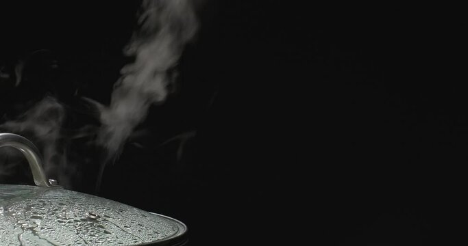 Steam rising from boiling water in saucepan on black background. Vapor from pot while cooking. Slow motion