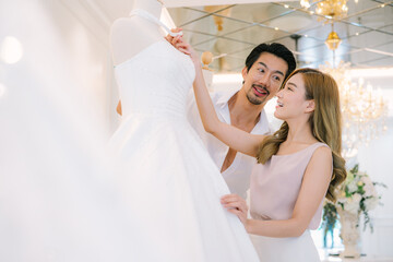 Naklejka premium Attractive Bride and groom is smiling while choosing wedding dress in modern wedding salon.