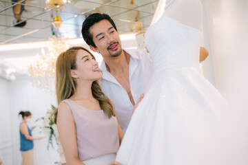 Attractive Bride and groom is smiling while choosing wedding dress in modern wedding salon.