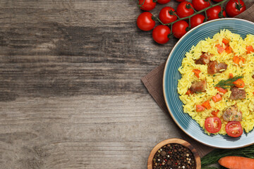 Delicious pilaf with meat and ingredients on wooden table, flat lay. Space for text