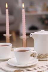 Cups of tea, teapot and burning candles on white table indoors