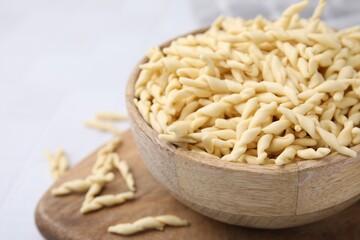Bowl with uncooked Italian trofie pasta on white table, closeup. Space for text